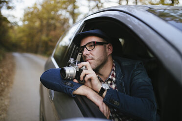 Mann hält Kamera und schaut weg, während er im Auto fährt - CAVF53069