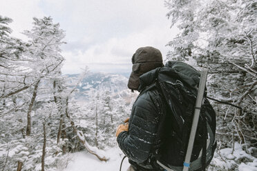 Rucksacktourist in warmer Kleidung im Winter im Wald stehend - CAVF53087