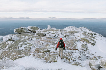 Rear view of backpacker with camera walking on snow covered rocks - CAVF53092