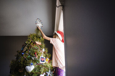Niedriger Blickwinkel eines Mädchens beim Schmücken des Weihnachtsbaums zu Hause - CAVF53096