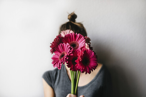 Frau hält rosa Blumen, während sie an einer weißen Wand zu Hause steht, lizenzfreies Stockfoto