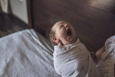 Mittelteil einer Mutter, die ihre neugeborene, gähnende Tochter auf dem Bett zu Hause trägt - CAVF53109