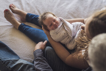 Draufsicht auf Eltern mit neugeborener Tochter, die zu Hause auf dem Bett sitzt - CAVF53112