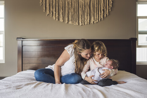 Mutter betrachtet ein kleines Mädchen, das von ihrer Tochter auf dem Bett zu Hause getragen wird, lizenzfreies Stockfoto