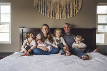 Portrait of happy parents with daughters sitting on bed at home - CAVF53114