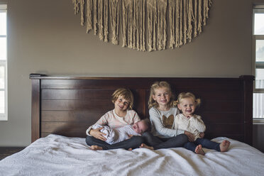 Porträt von lächelnden Schwestern mit Baby-Mädchen sitzen auf dem Bett zu Hause - CAVF53115