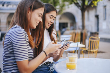 Freunde benutzen Mobiltelefone, während sie in einem Straßencafé sitzen - CAVF53122