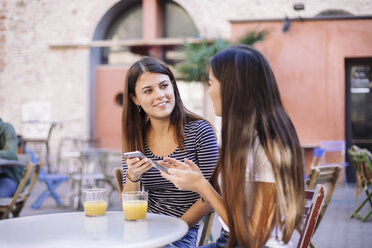 Friends talking while using mobile phones at sidewalk cafe - CAVF53123