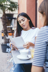 Frau liest Dokumente, während sie mit einem Freund am Tisch eines Straßencafés sitzt - CAVF53128