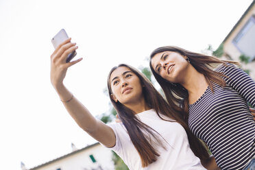 Niedriger Blickwinkel von Freunden, die ein Selfie mit ihrem Mobiltelefon machen, während sie vor einem klaren Himmel stehen - CAVF53132