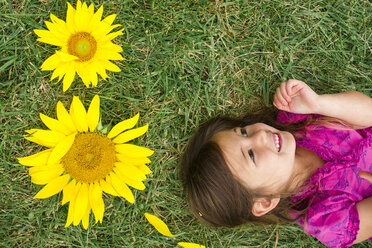 Hohe Winkel Ansicht der niedlichen glückliches Mädchen liegt von Sonnenblumen auf grasbewachsenen Feld - CAVF53151