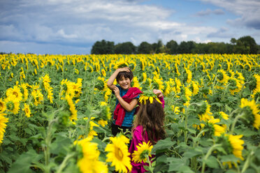 Geschwister spielen mit Sonnenblumen, während sie auf dem Bauernhof gegen den bewölkten Himmel stehen - CAVF53153