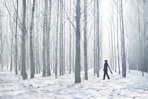 Full length of young man wearing black warm clothing while walking amidst trees at forest during foggy weather stock photo