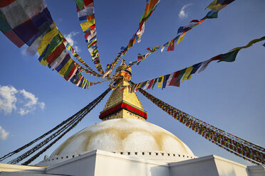 Low angle view of Boudhanath stupa with colorful prayer flags against blue sky - CAVF53168