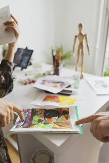 Frauenhände, die auf ein Gemälde am Schreibtisch in einem Atelier zeigen - AFVF01913