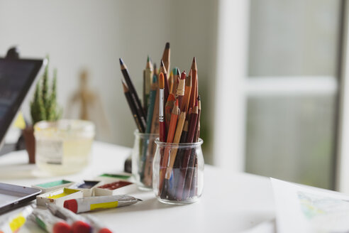Gläser mit Buntstiften, Farbtuben und Aquarellfarben auf dem Arbeitstisch eines Illustrators in einem Atelier - AFVF01919