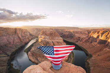 USA, Arizona, Colorado River, Horseshoe Bend, junger Mann auf Aussichtspunkt mit amerikanischer Flagge - KKAF02845