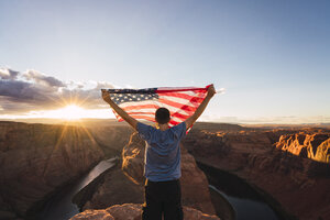 USA, Arizona, Colorado River, Horseshoe Bend, junger Mann auf Aussichtspunkt mit amerikanischer Flagge - KKAF02847