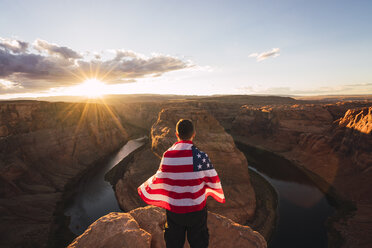 USA, Arizona, Colorado River, Horseshoe Bend, junger Mann auf Aussichtspunkt mit amerikanischer Flagge - KKAF02848