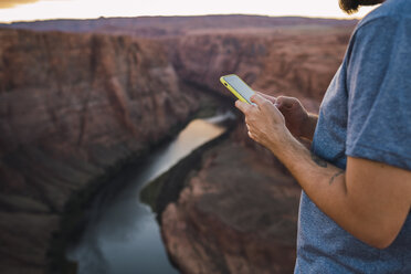 USA, Arizona, Colorado River, Horseshoe Bend, junger Mann auf Aussichtspunkt mit Smartphone - KKAF02852
