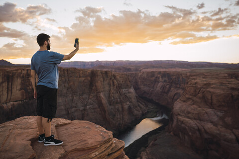 USA, Arizona, Colorado River, Horseshoe Bend, young man on viewpoint using smartphone, photographing stock photo