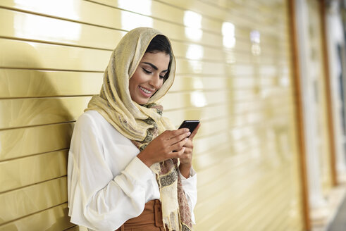 Spanien, Granada, junge arabische Touristin mit Hidschab, die ein Smartphone benutzt - JSMF00547