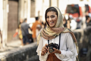 Spain, Granada, young Arab tourist woman wearing hijab, using camera during sightseeing in the city - JSMF00557