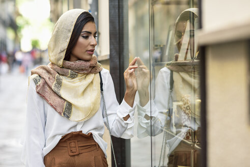 Spanien, Granada, junge muslimische Touristin, die einen Hijab trägt und Schaufenster in einer Einkaufsstraße betrachtet - JSMF00558