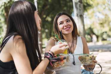 Girl friends sitting in a park, eating salad - KKAF02864