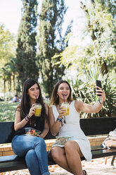 Freundinnen, die in einem Park sitzen, Salat essen, Saft trinken und Selfies machen - KKAF02869