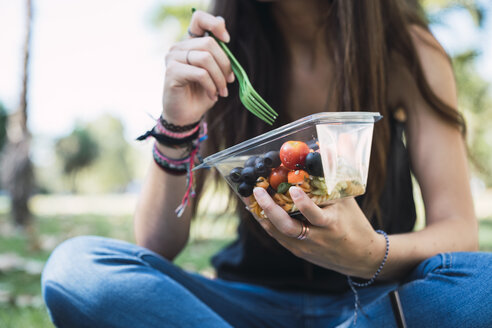 Junge Frau, die in einem Park sitzt und Salat isst - KKAF02874
