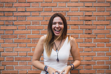 Porträt einer lachenden jungen Frau vor einer Backsteinmauer - KKAF02880