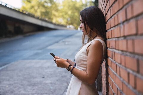Junge Frau vor einer Backsteinmauer mit Smartphone, lizenzfreies Stockfoto