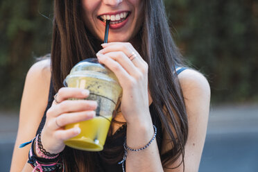 Smiling woman drinking juice with a straw - KKAF02882