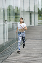 Young woman running along building in the city - FMGF00087