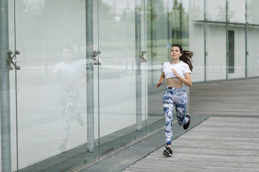 Junge Frau läuft an einem Gebäude in der Stadt entlang - FMGF00088