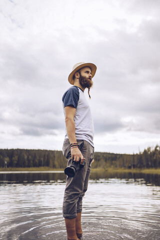 Schweden, Lappland, Mann mit Kamera steht im Wasser und schaut in die Ferne, lizenzfreies Stockfoto