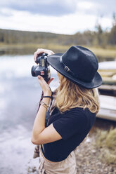 Schweden, Lappland, junge Frau mit schwarzem Hut beim Fotografieren mit Kamera - RSGF00035