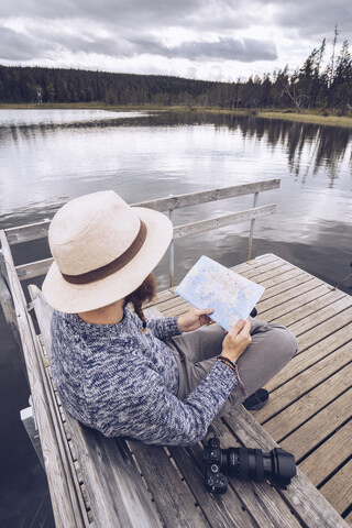 Schweden, Lappland, Mann mit Kamera sitzt auf einer Bank auf einem Steg und schaut auf eine Karte, lizenzfreies Stockfoto