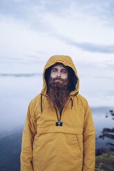Sweden, Lapland, portrait of young man with full beard wearing yellow windbreaker in nature - RSGF00043