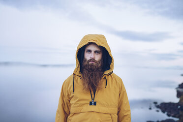 Sweden, Lapland, portrait of serious man with full beard wearing yellow windbreaker - RSGF00044