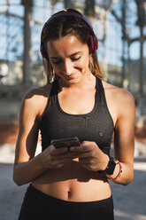 Fitte junge Frau mit einer Smartwatch, die ein Smartphone benutzt - KKAF02916
