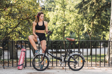 Fit junge Frau mit Fahrrad, lehnt sich an Geländer in einem Park - KKAF02926