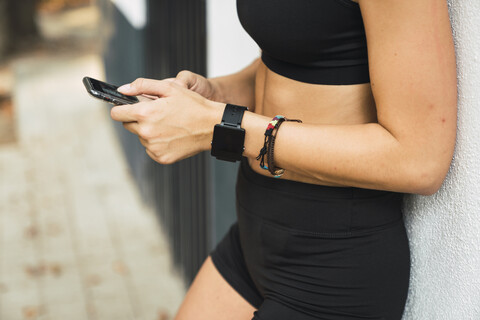 Fitte junge Frau mit einer Smartwatch, die ein Smartphone benutzt, lizenzfreies Stockfoto