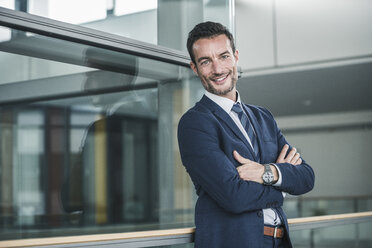 Portrait of a successful businessman, standing in office building, with arms crossed - UUF15793