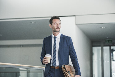 Businessman with briefcase walking in office building, holding cup of coffee - UUF15796