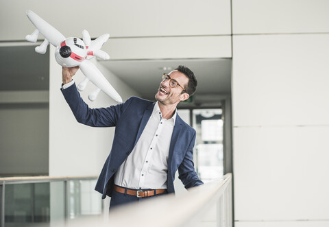 Lachender Geschäftsmann, der mit einem Spielzeugflugzeug im Bürogebäude spielt, lizenzfreies Stockfoto