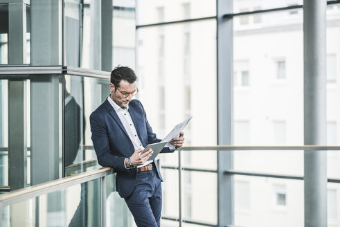 Geschäftsmann, der in einem Bürogebäude steht und ein digitales Tablet benutzt - UUF15802