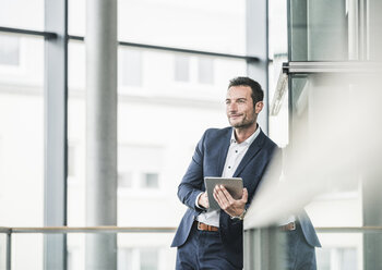 Businessman standing in office building, using digital tablet - UUF15804