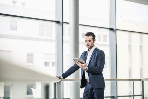 Geschäftsmann, der in einem Bürogebäude steht und ein digitales Tablet benutzt - UUF15805